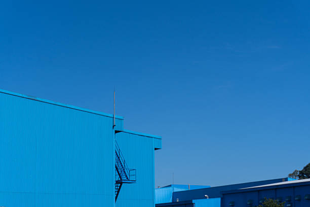 A stark azure building stretches upwards, its metal facade punctuated by the geometric zig-zag of external stairs against a clear blue sky, presenting an industrial elegance