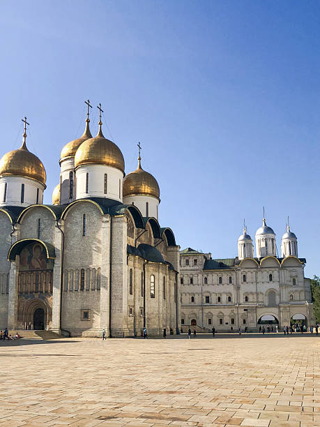 The historic Assumption Cathedral, part of the Moscow Kremlin complex in Russia, on a sunny summer day. The cathedral's iconic golden domes shine against a vivid blue sky.