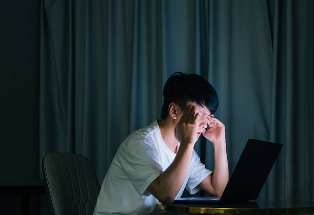 istock Young Asian man sitting at home at night using a computer with hand on his head, showing anxiety, worry, and stress, reflecting emotional struggle, mental pressure, and overwork in modern urban lifestyle. 2243600492