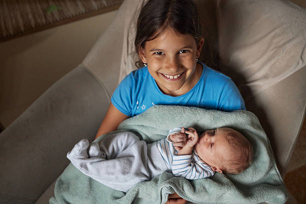 Older sister gently cradling her new baby brother wrapped in a blanket