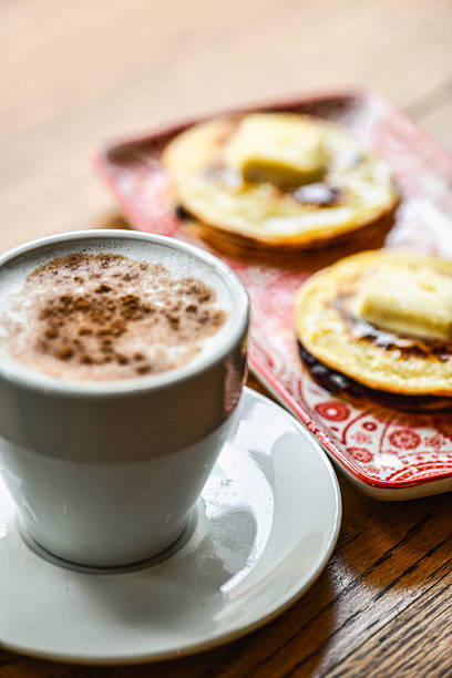 A cozy breakfast scene featuring a foamy cappuccino dusted with cinnamon, two buttered pancakes, fresh berries, and a warm wooden table, perfect for café menus and brunch promotions.