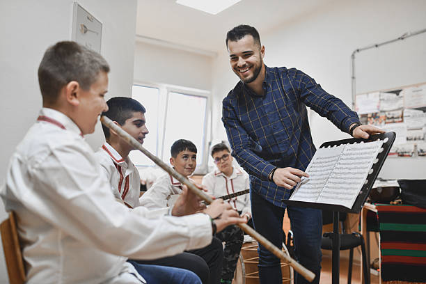 istock Male Instructor Pointing At Sheet Music While Helping Boys Play Various Traditional Instruments 2243607155