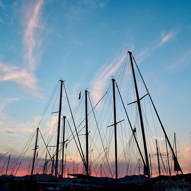 A tranquil harbor at sunset with colorful clouds and a vibrant red-orange sky reflecting on the calm water, framed by silhouettes of docked sailboats. High quality photo