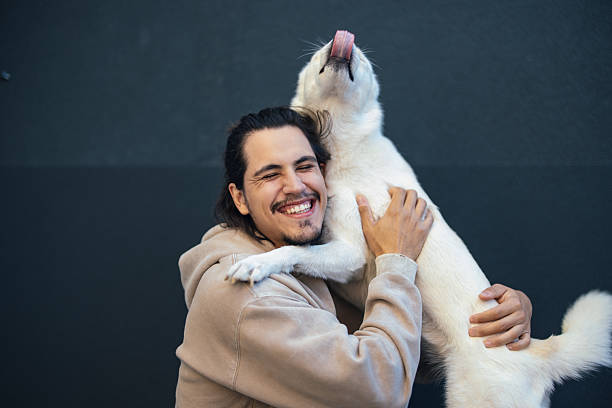 oyful man sitting and hugging his playful white dog, smiling with affection.