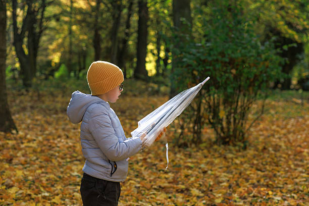 Boy in hat and jacket stands in warm backlight holding a closed umbrella. Concept of golden hour, mindfulness and quiet autumn moment.