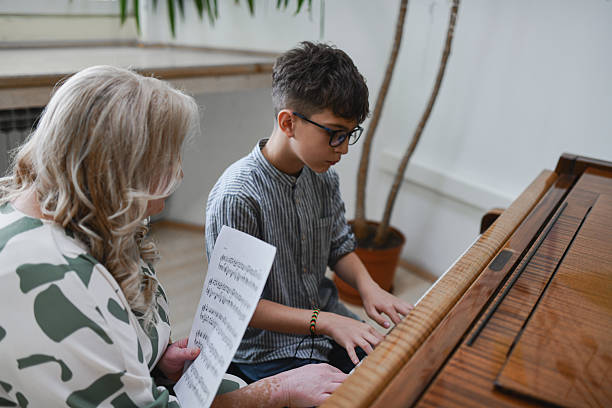istock Teenage Boy Looking Focused While Practicing Piano Piece and Teacher is Observing Him Closely 2243613532