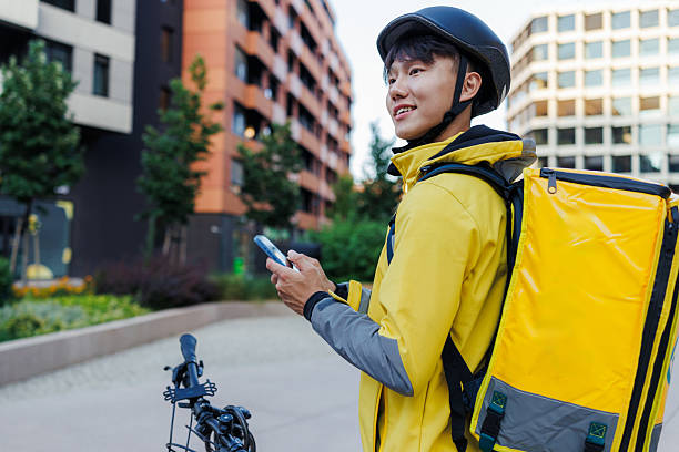 istock Chinese delivery man in yellow jacket, using a smartphone outdoors in an urban area 2243617248