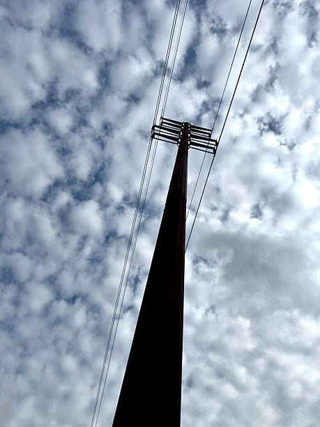 Vertical wide angle tall metal power line pole under cloudy sky