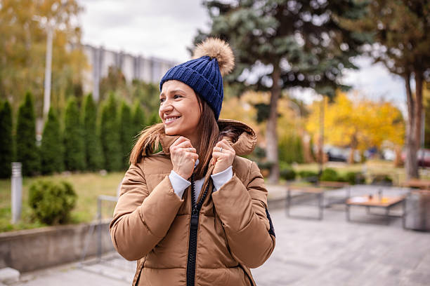 Two adults are outside dressed warmly in jackets and hats. They are coughing and sneezing, showing signs of illness while trying to enjoy the fall weather.