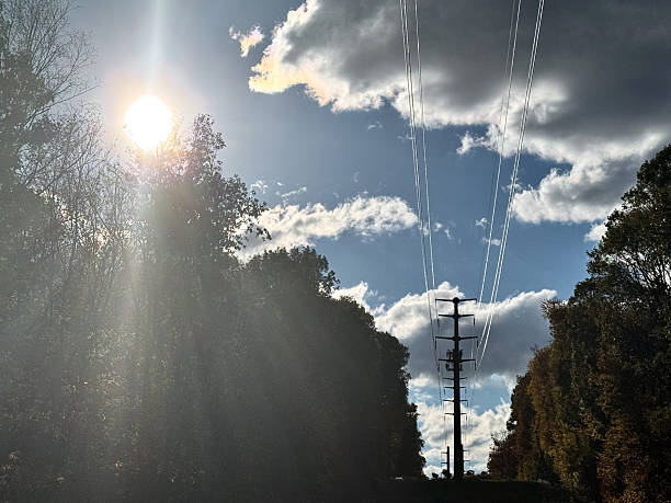 EX WS tall metal power line pole with sun and clouds in silhouette
