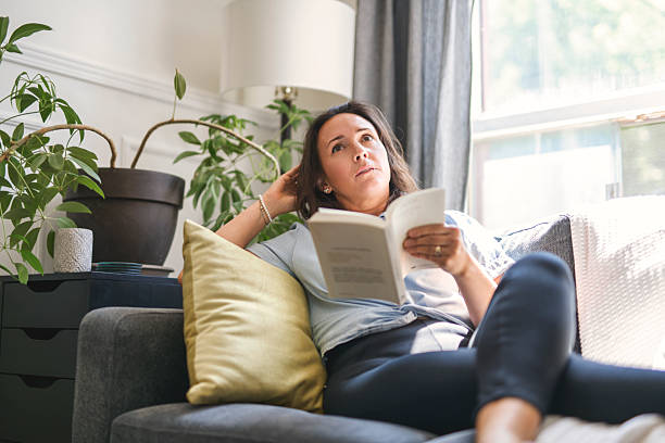 istock woman sitting and reading book on a sofa at home 2243628111