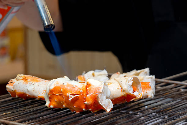 istock King Crab legs grilling over open flame. Split shells reveal white meat, with a gloved hand using tongs to adjust pieces. Dim lighting highlights the crab's vivid red and orange tones, evoking a street food vibe. 2243629828