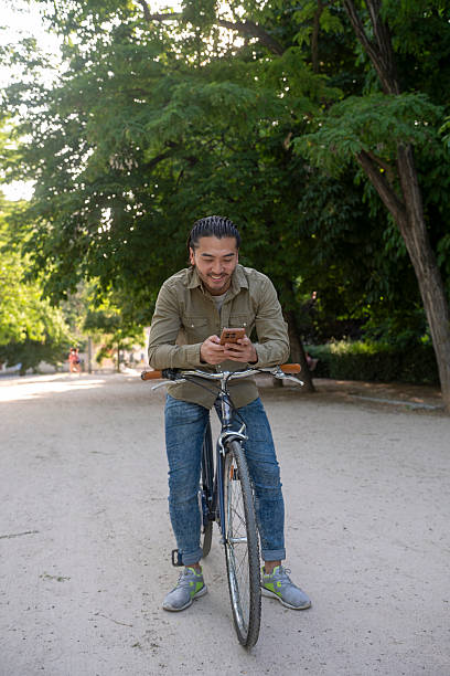 istock Young asian man using phone on bicycle in park 2243631825
