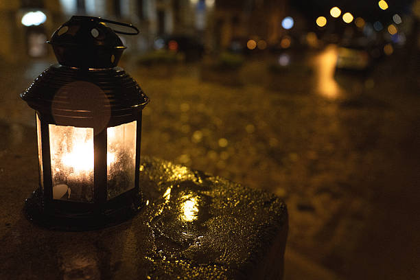 istock Lantern with candle glowing on wet stone at night  warm light reflection on rainy cobblestone street creating cozy and atmospheric urban mood 2243633185