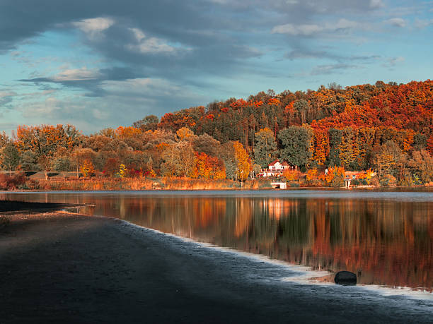 Scenic autumn landscape with vibrant forest reflecting on calm lake water at sunset. Peaceful nature scenery ideal for travel, relaxation, and seasonal background concepts.