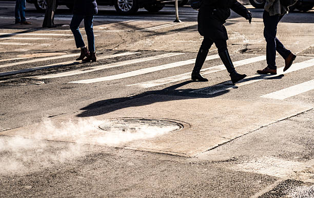 Steam rising from a Manhattan manhole cover as pedestrians commute to work, early in the morning.