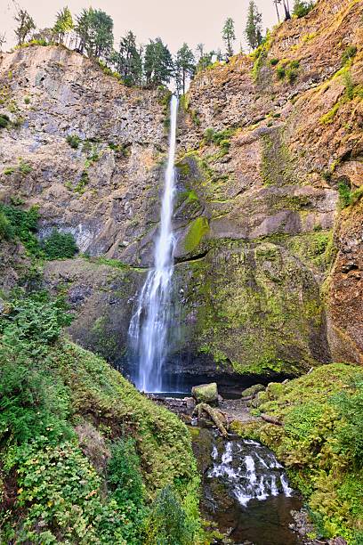 istock Waterfall cascading down a rocky cliff with lush greenery. 2243643125