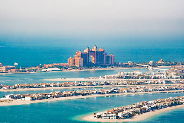 Dubai, UAE - January 23, 2024: Atlantis Hotel on the Palm Jumeirah island with flag poles, palm trees and flowers in the foreground