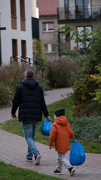 istock Father and son carrying blue bags while walking along city path 2243660394