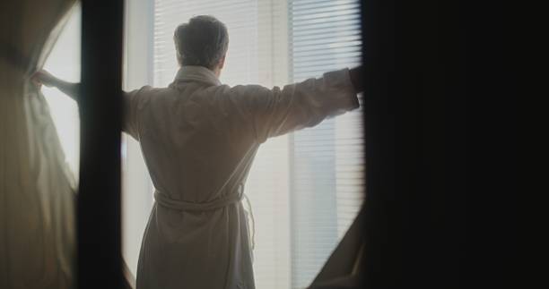 istock Senior Man Enjoys First Rays of Morning Sun Through Large Hotel Windows 2243661062