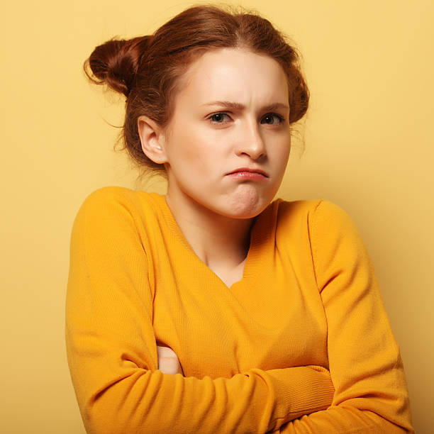 istock frowning young woman thinking on yellow background 2243661696