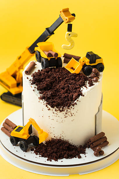 istock Birthday cake for five year old kid, decorated with construction vehicles. Heavy car themed homemade cake for toddler boy birthday celebration with toy excavators and crane on the yellow background. 2243662042