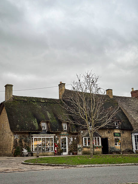 Broadway, Worcestershire, UK – December 21, 2023: Street view of Whatever the Weather gift shop and The Cotswold Chocolate Company in Broadway village, both housed in traditional Cotswold stone cottages decorated with Christmas lights and festive displays during the holiday season.