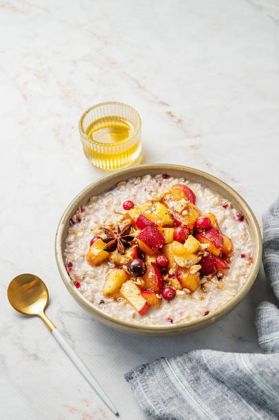 Overnight oatmeal with apple, cranberry and cinnamon in a plate on a marble background with honey
