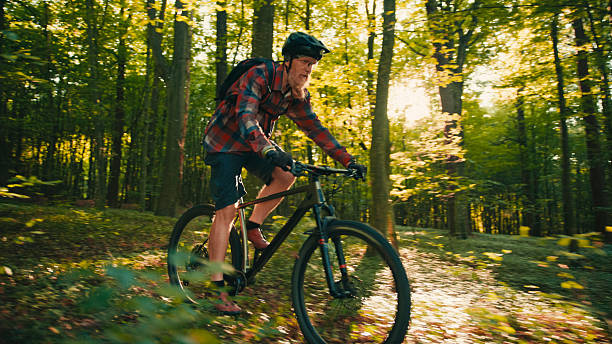 istock Confident Mature Biker Cycling Through Sunlit Forest Trail with Determination 2243665372