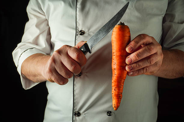 istock A chef holds a bright orange carrot in one hand while using a sharp knife in the other hand, preparing for a meal in a professional kitchen setting 2243666521