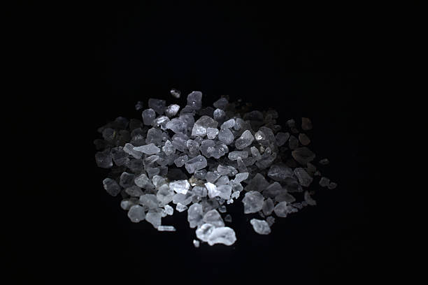 A pile of sea salt with large crystals lies on a black background.