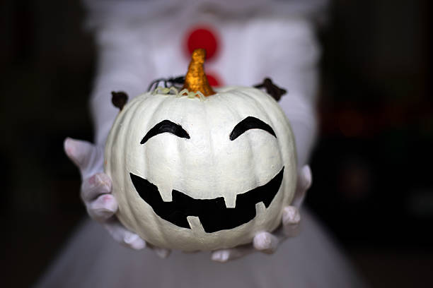 Girl's hands holding a funny white Halloween pumpkin with a blurred black background