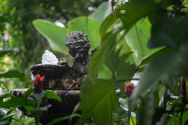 A charming garden fountain adds tranquility to a lush green landscape. The serene statue surrounded by vibrant foliage creates a peaceful outdoor atmosphere.