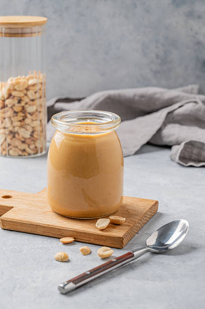 istock Creamy peanut butter in a jar on a wooden board on a blue background 2243672905