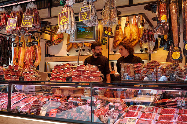 Barcelona, Spain - June 10, 2025: vendors with customers at La Boqueria market, one of the oldest in Europe. At the market is possible to purchase vegetables, fruits, seafood, snack, spanish delicacies, salami, tapas and ready-to-eat meals.
