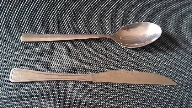 istock Bread knife and metal spoon on a dark nylon towel 2243674743