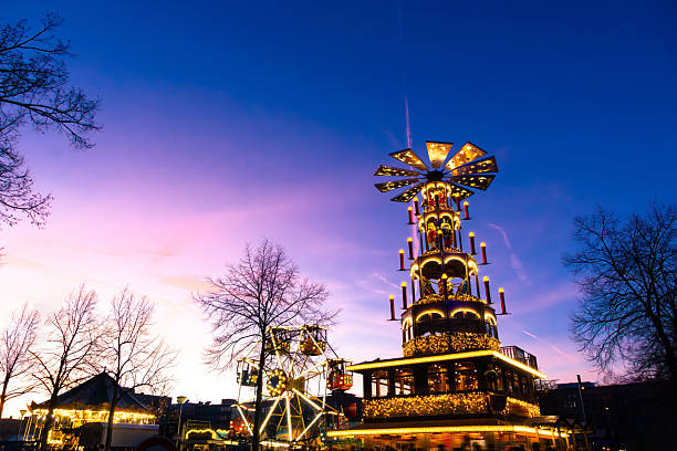 A towering, multi-tier festival float with warm lights and candles in the evening. Festive traditional German Christmas market setting in Mannheim, Germany.