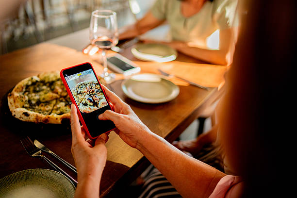 istock Woman photographing pizza using mobile phone at restaurant - mobile device screen on focus 2243681712