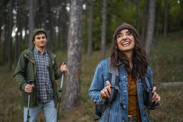 Young woman smiling brightly while enjoying a forest walk with her partner, carrying a backpack and embracing the refreshing outdoors during their journey