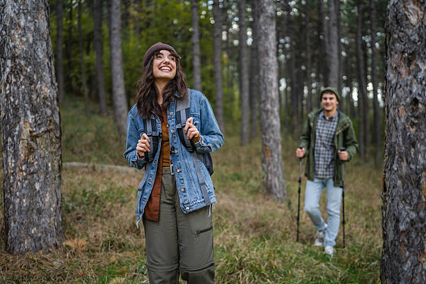 Young couple enjoying an active outdoor adventure, hiking through a dense forest with backpacks and poles, smiling and finding happiness exploring nature together
