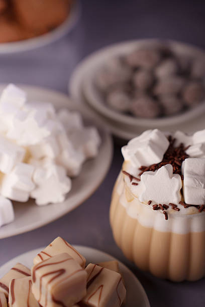 istock cozy kitchen scene with a warm drink topped with marshmallows and chocolate sprinkles, surrounded by plates of assorted chocolates, cookies, and marshmallow treats on a soft purple surface, elegant 2243687424