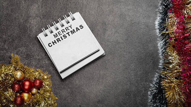 istock Greeting of Merry Christmas text in a notepad on a black background. Mockup or Copy space. Holiday greetings or winter themes. Concept of the Merry Christmas celebration 2243688294