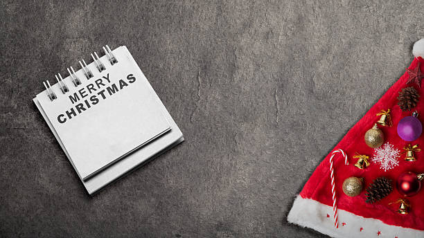 istock Greeting of Merry Christmas text in a notepad on a black background. Mockup or Copy space. Holiday greetings or winter themes. Concept of the Merry Christmas celebration 2243688307