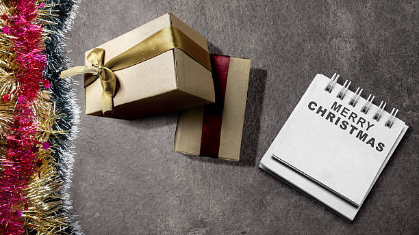 istock Greeting of Merry Christmas text in a notepad with gift boxes on a black background. Mockup or Copy space. Holiday greetings or winter themes. Concept of the Merry Christmas celebration 2243688332