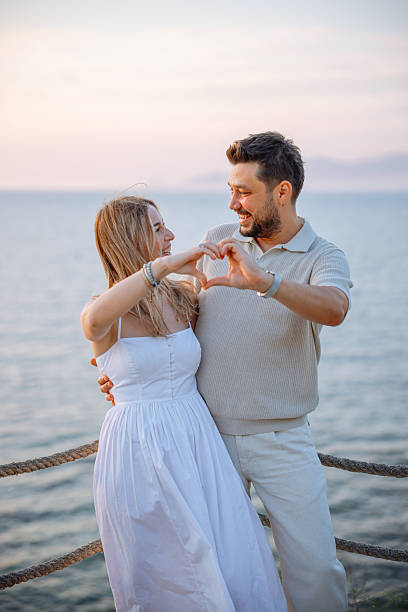 Happy and loving mature caucasian couple enjoying a romantic date at the beach together on a sunny day. Cheerful affectionate husband hugging arm around wife while bonding on vacation outdoor