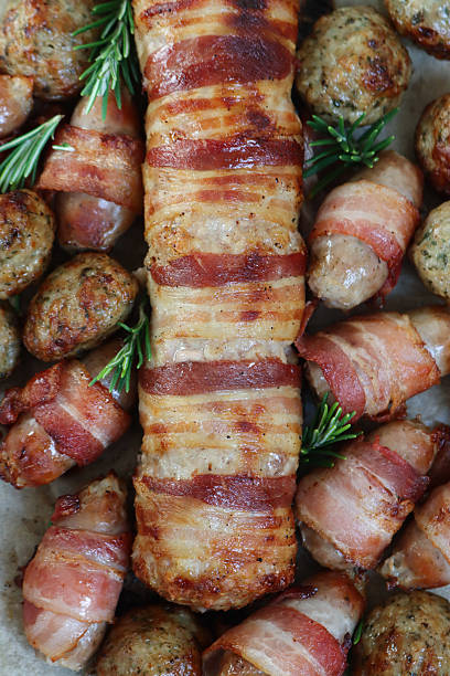 istock Full frame image of Christmas dinner ingredients, pigs in blankets (pork sausages wrapped in bacon) and stuffing meatballs on greaseproof parchment paper lined oven tray, Rosemary sprigs, elevated view 2243689331