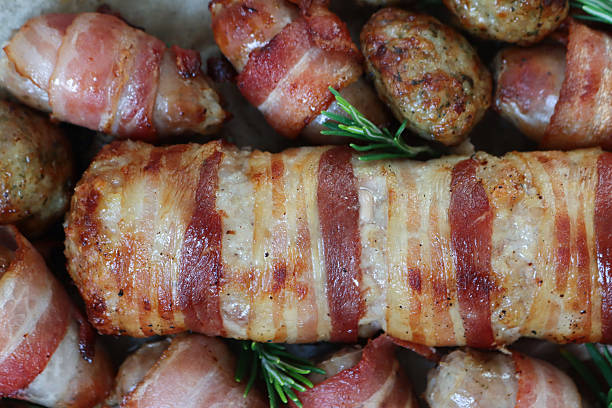 istock Full frame image of Christmas dinner ingredients, pigs in blankets (pork sausages wrapped in bacon) and stuffing meatballs on greaseproof parchment paper lined oven tray, Rosemary sprigs, elevated view 2243689362