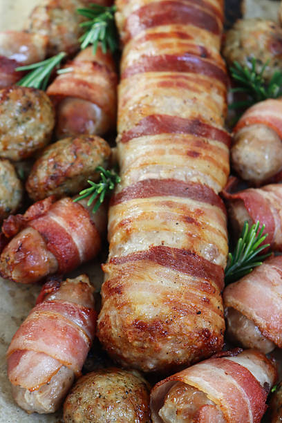 istock Full frame image of Christmas dinner ingredients, pigs in blankets (pork sausages wrapped in bacon) and stuffing meatballs on greaseproof parchment paper lined oven tray, Rosemary sprigs, elevated view 2243689366