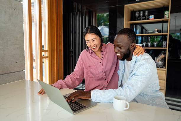 istock Young happy multiethnic couple having fun while using laptop at home. Happy couple discussing future 2243692469