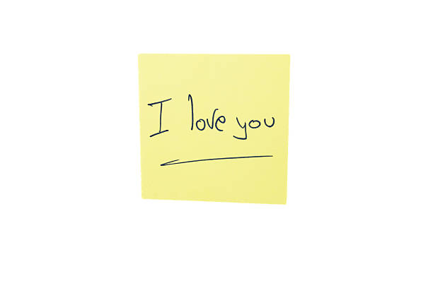 istock Yellow sticky note with romantic handwritten message in English on a plain white background. 2243693567